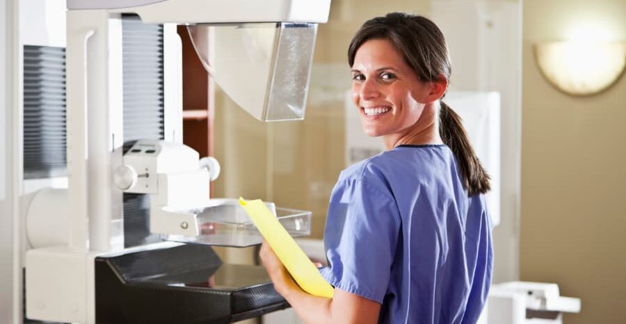 mammography technologist standing in front of machine smiling